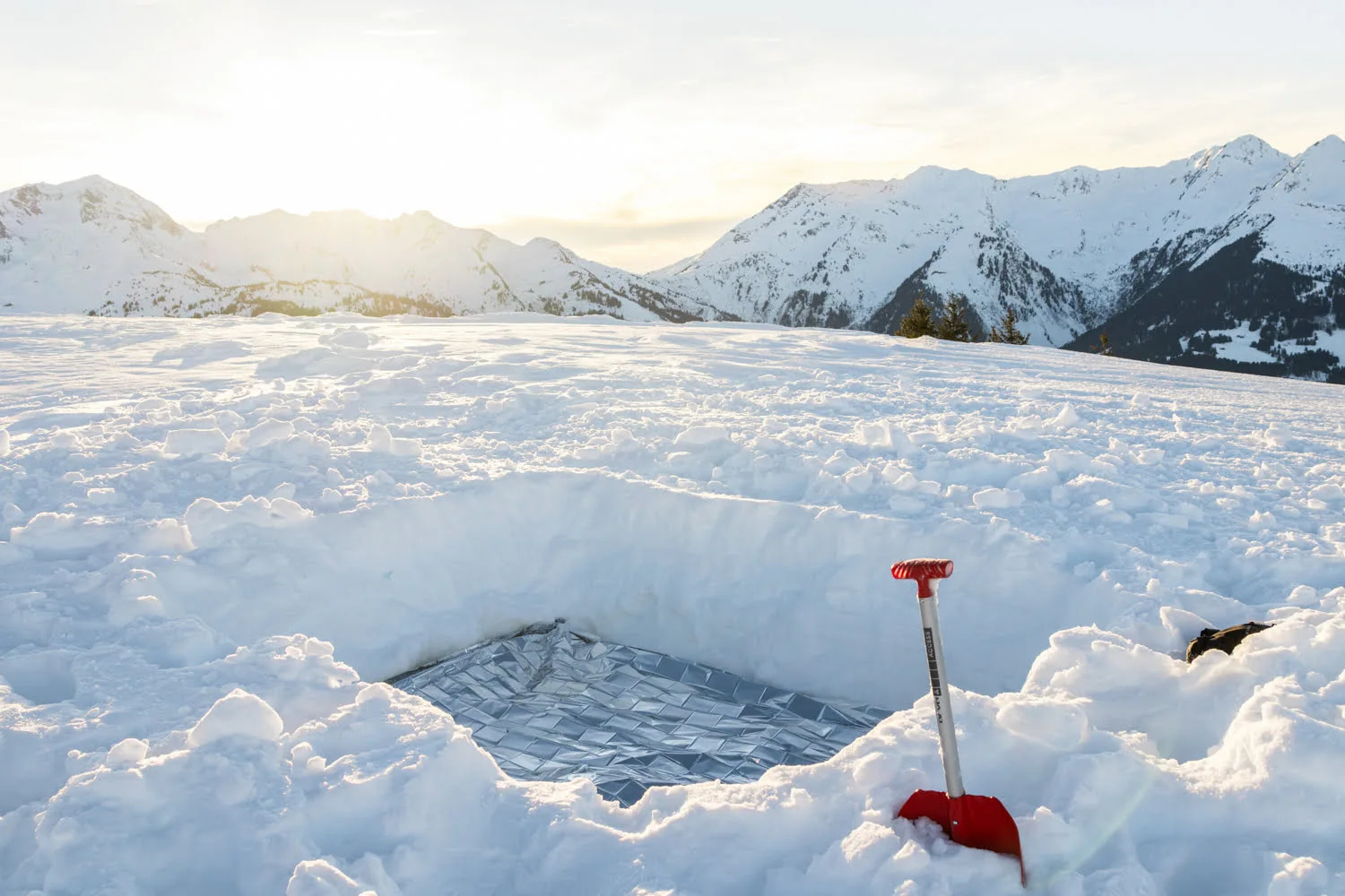 trou dans la neige pour bivouaquer avec couverture de survie
