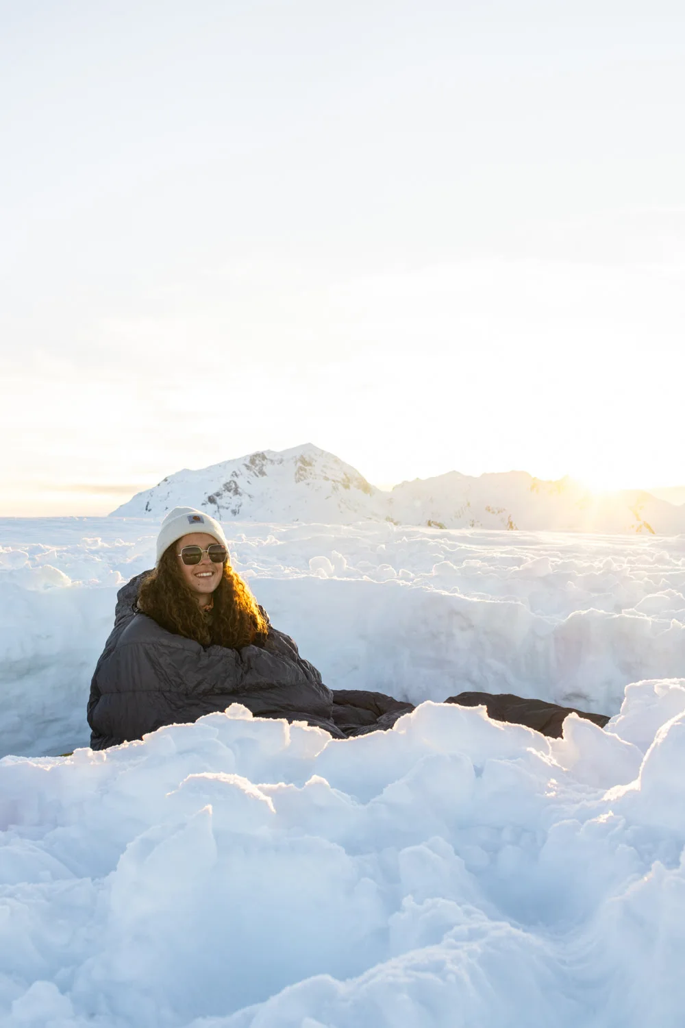femme dans un bivouac enneigé en montagne au coucher du soleil