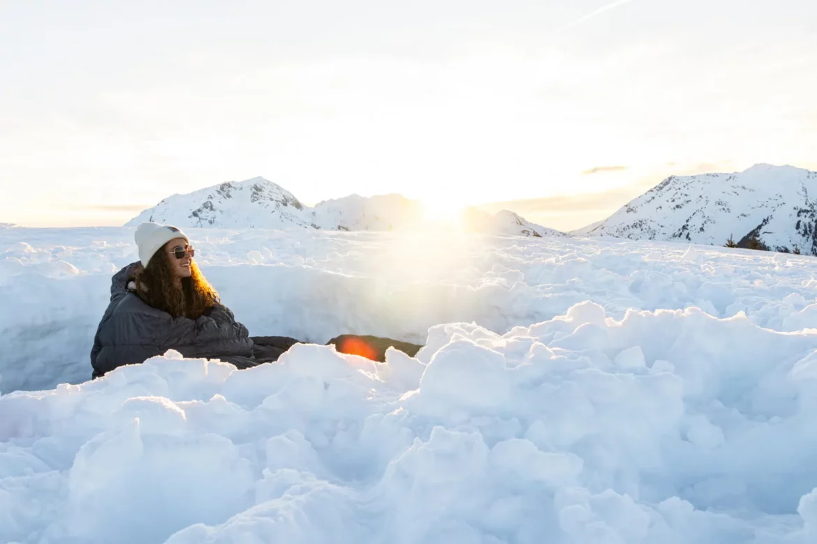 femme dans un bivouac enneigé en montagne au coucher du soleil