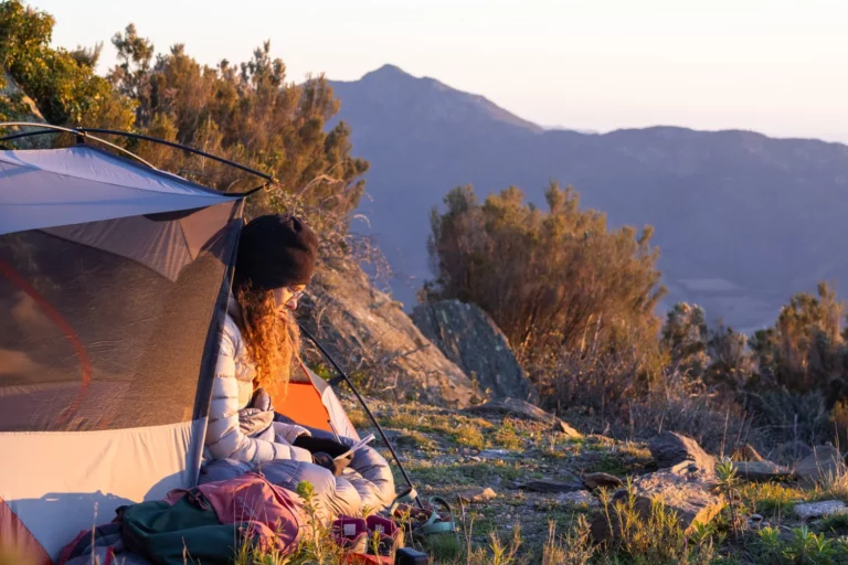 tente devant montagne avec randonneuse dedans au lever du soleil
