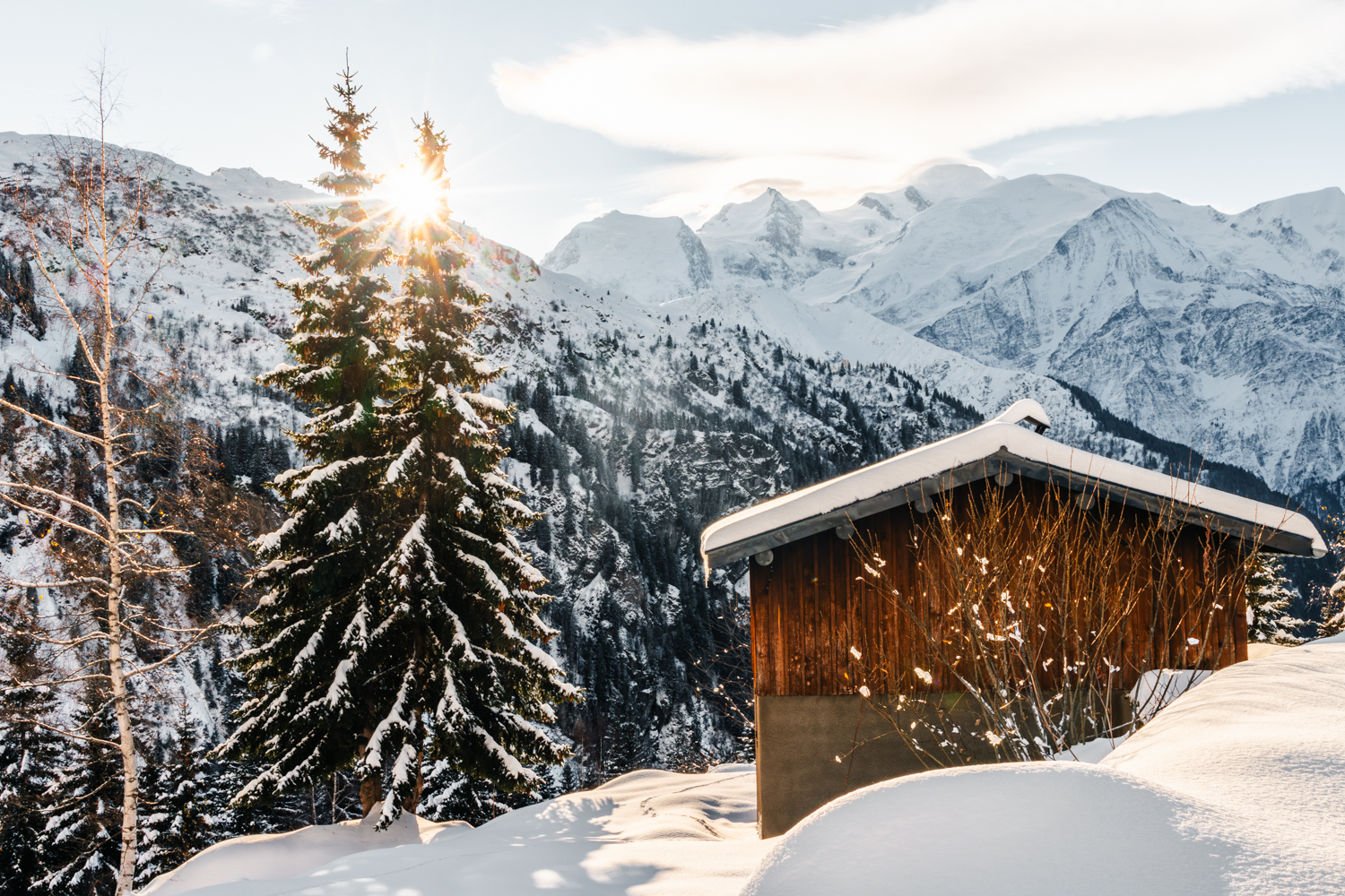 photo d'un Chalet traditionnel avec vue directe sur les sommets enneigés du massif du Mont-Blanc et le soleil. Format Paysage