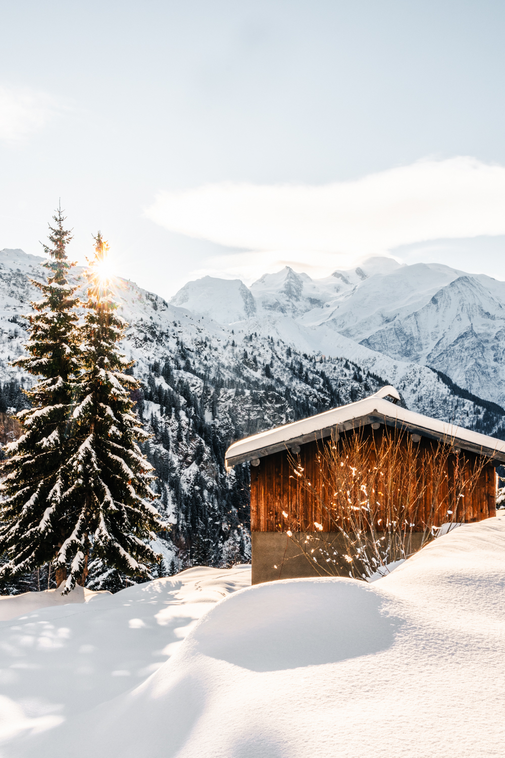 photo d'un Chalet traditionnel avec vue directe sur les sommets enneigés du massif du Mont-Blanc et le soleil. Format portrait