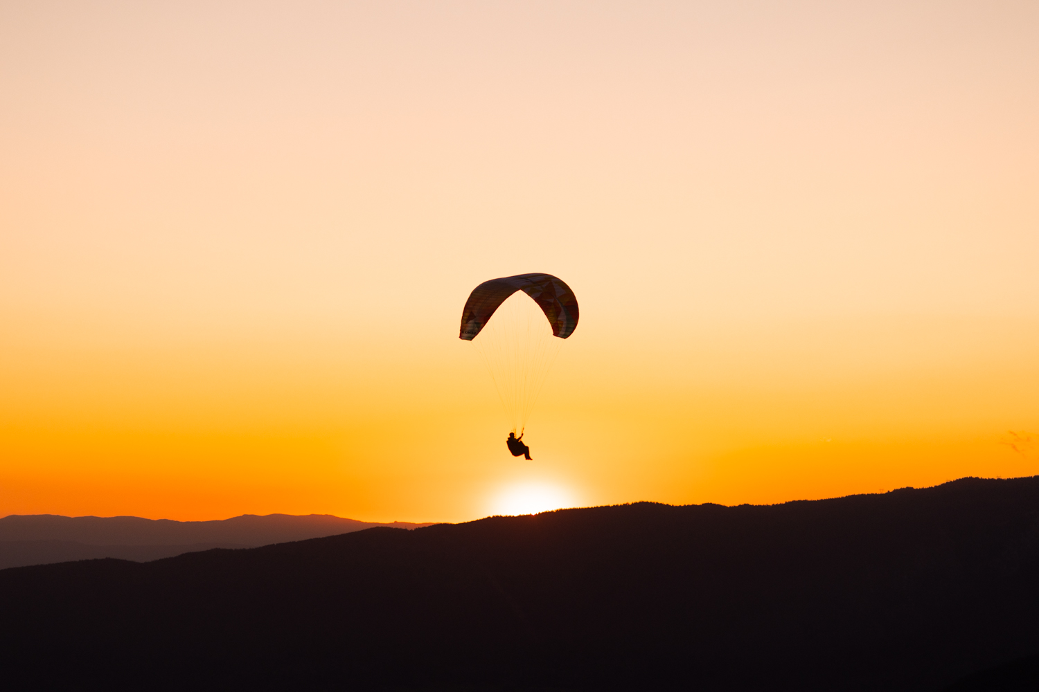 photo d'un Parapente évoluant dans le ciel orangé du coucher de soleil au-dessus des reliefs montagneux