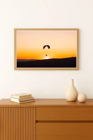 photo d'un Parapente évoluant dans le ciel orangé du coucher de soleil au-dessus des reliefs montagneux