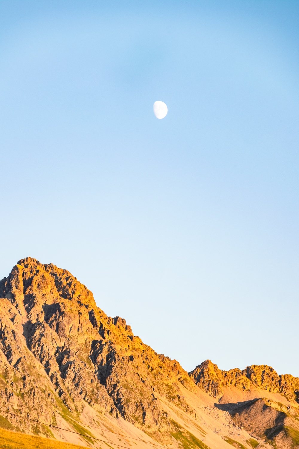 photo de lumières douces de fin de soirée baignant les sommets montagneux et la lune dans une atmosphère apaisante